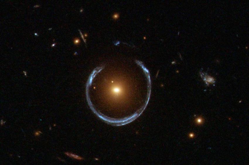 The newly discovered ultramassive blackhole lies at the centre of the orange galaxy. Far behind it is a blue galaxy that is being warped into the horseshoe shaped ring by distortions in spacetime created by the immense mass of the foreground orange galaxy.