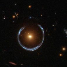 The newly discovered ultramassive blackhole lies at the centre of the orange galaxy. Far behind it is a blue galaxy that is being warped into the horseshoe shaped ring by distortions in spacetime created by the immense mass of the foreground orange galaxy.