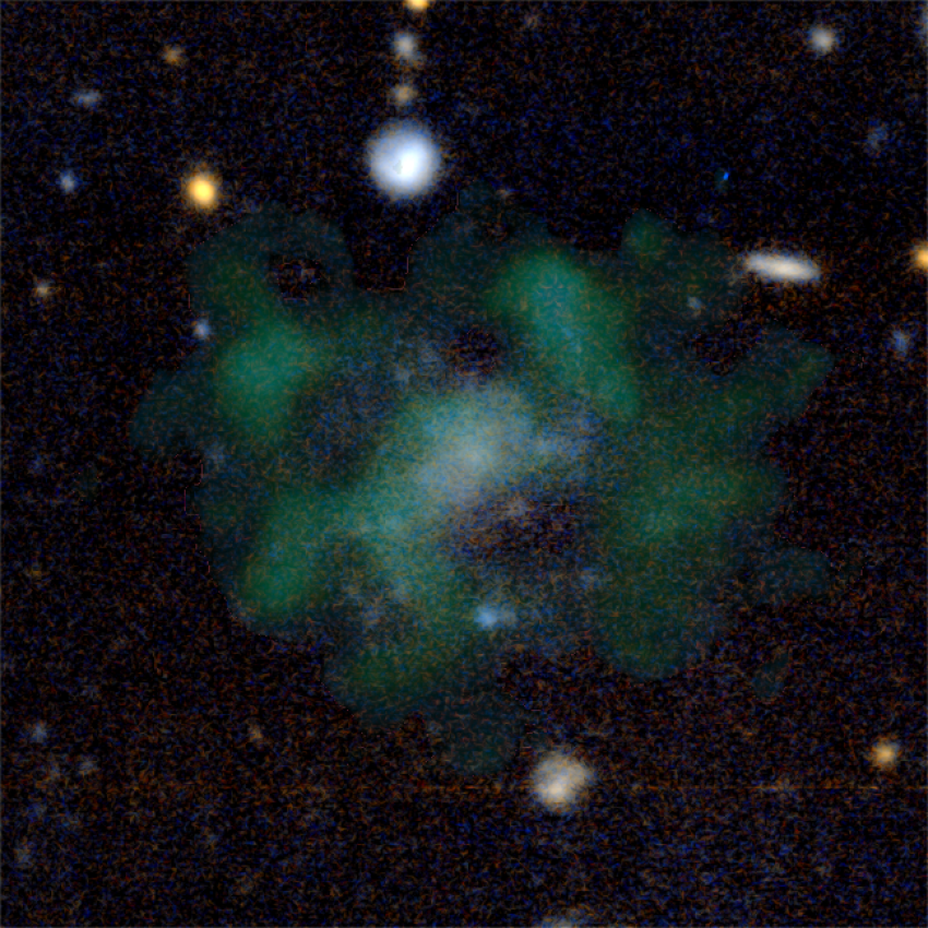 A diffuse galaxy in green and blue hues. White and orange stars appear around the clouds of the galaxy.